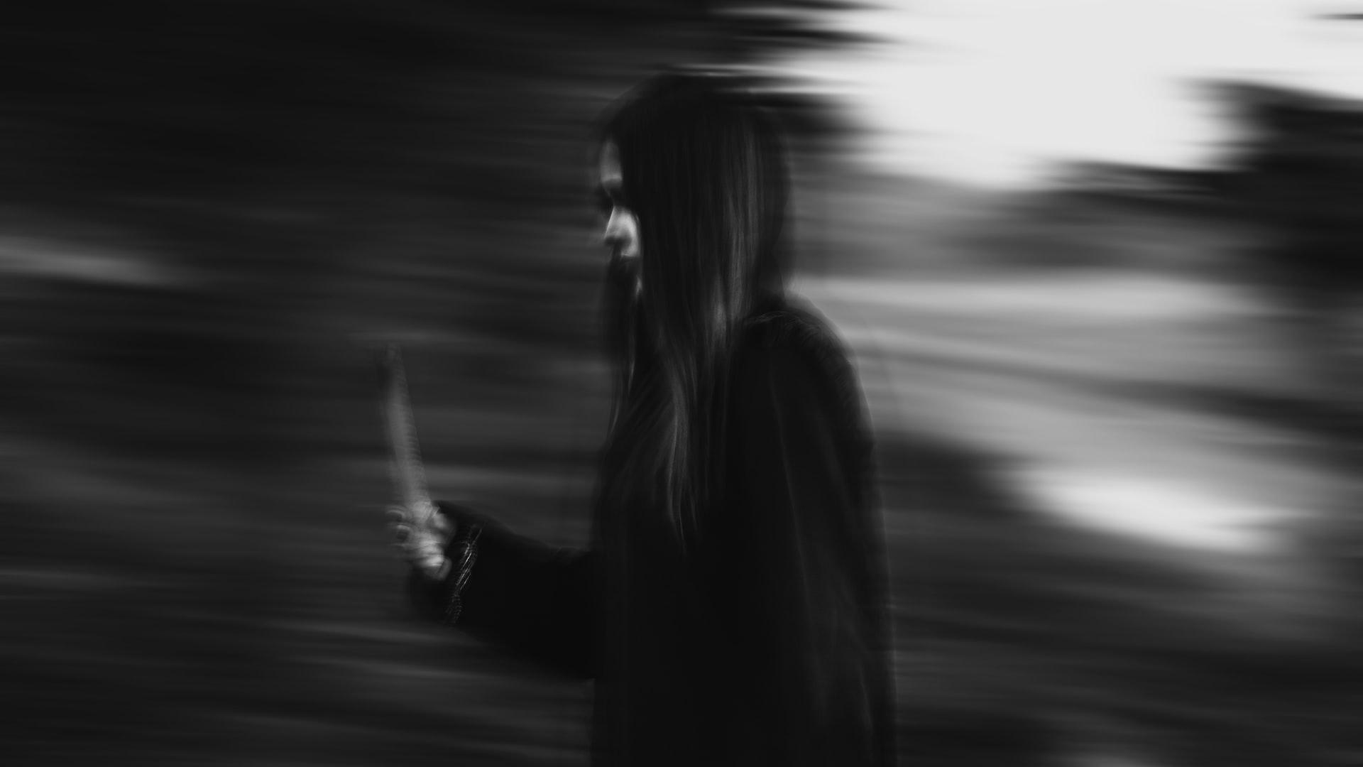 Blurry photo of person in black hoodie with long black hair, possibly carrying a knife.